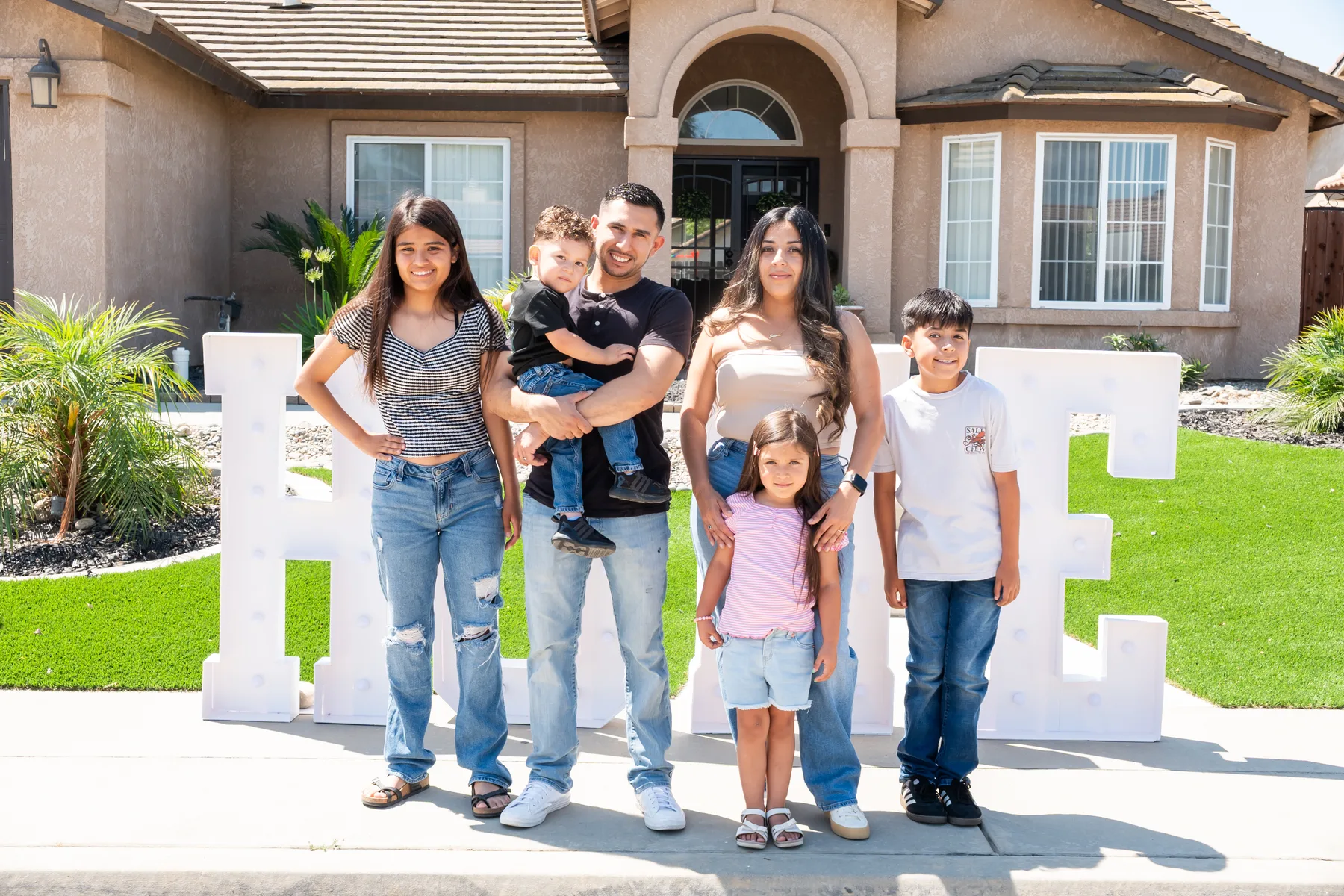 Group poses beside a large HOME sign outside a house.