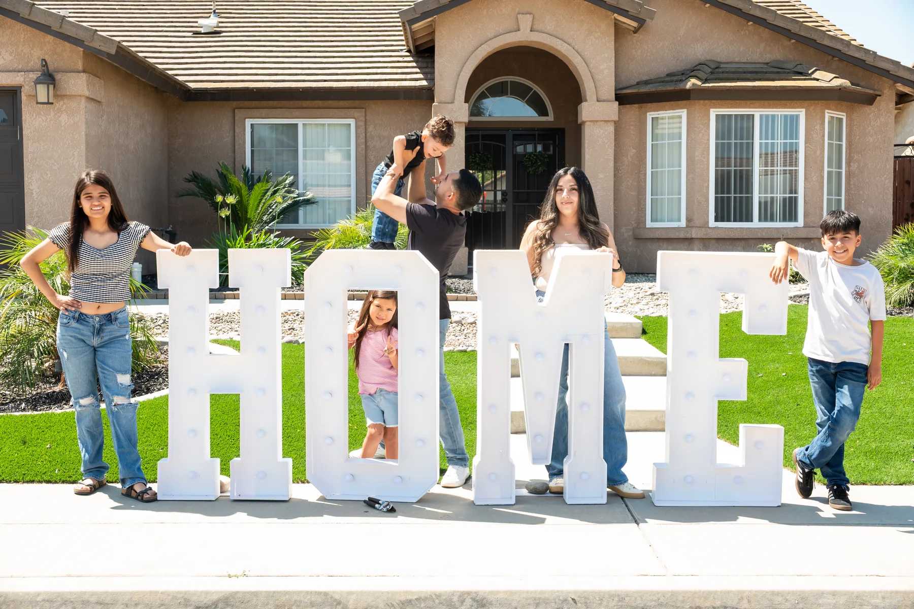 Group celebrates beside a HOME sign in front of the house.