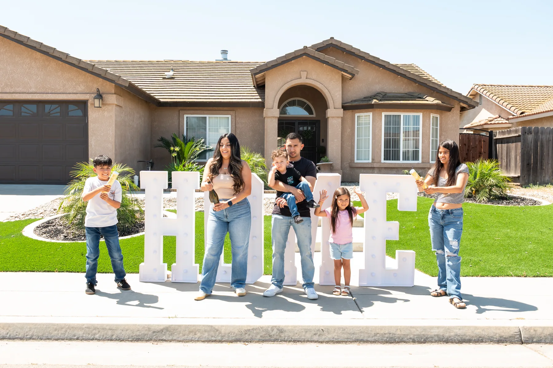 Group gathers around a HOME sign in front of the house.