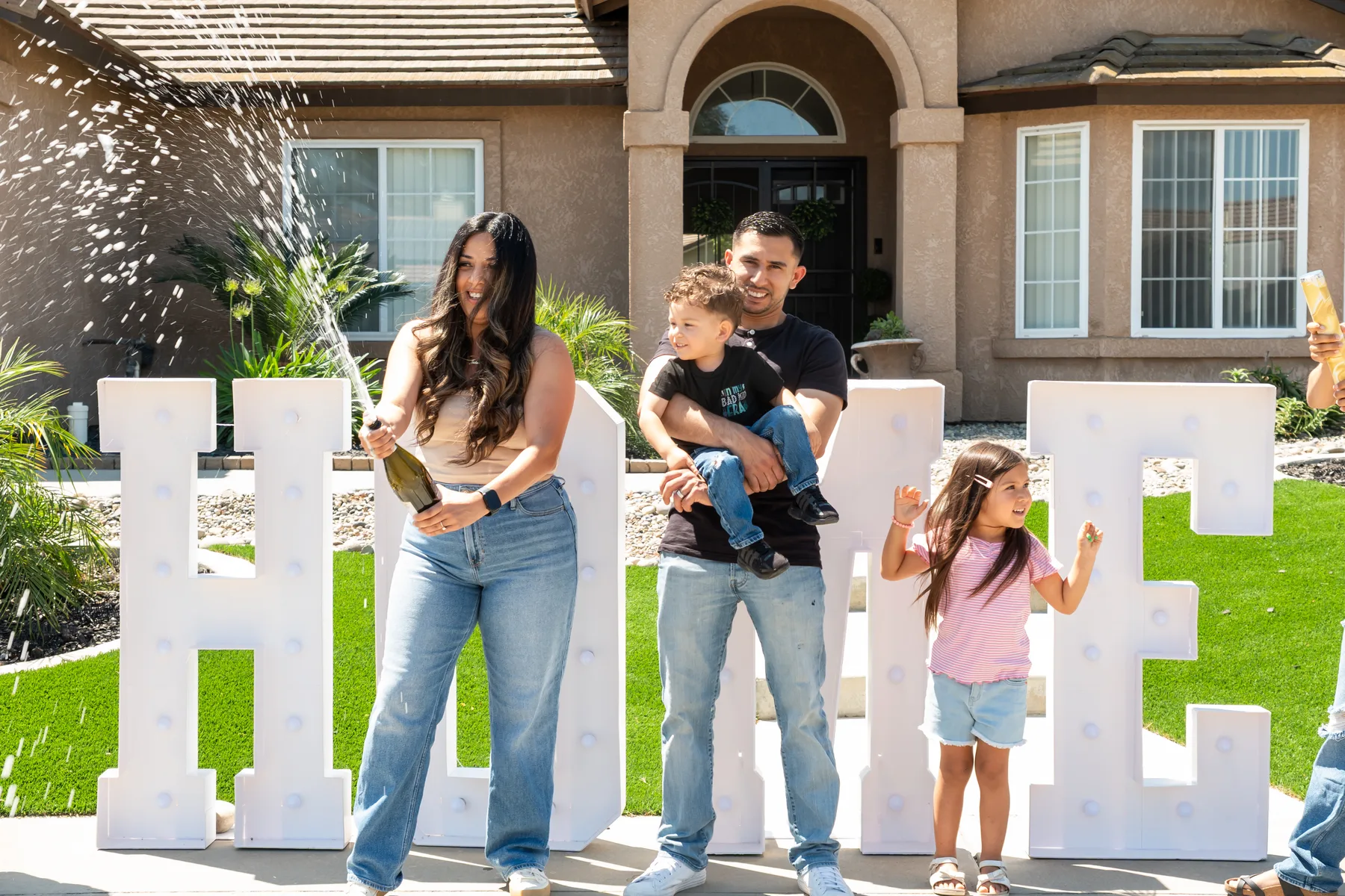 Group celebrates beside a HOME sign on the lawn.