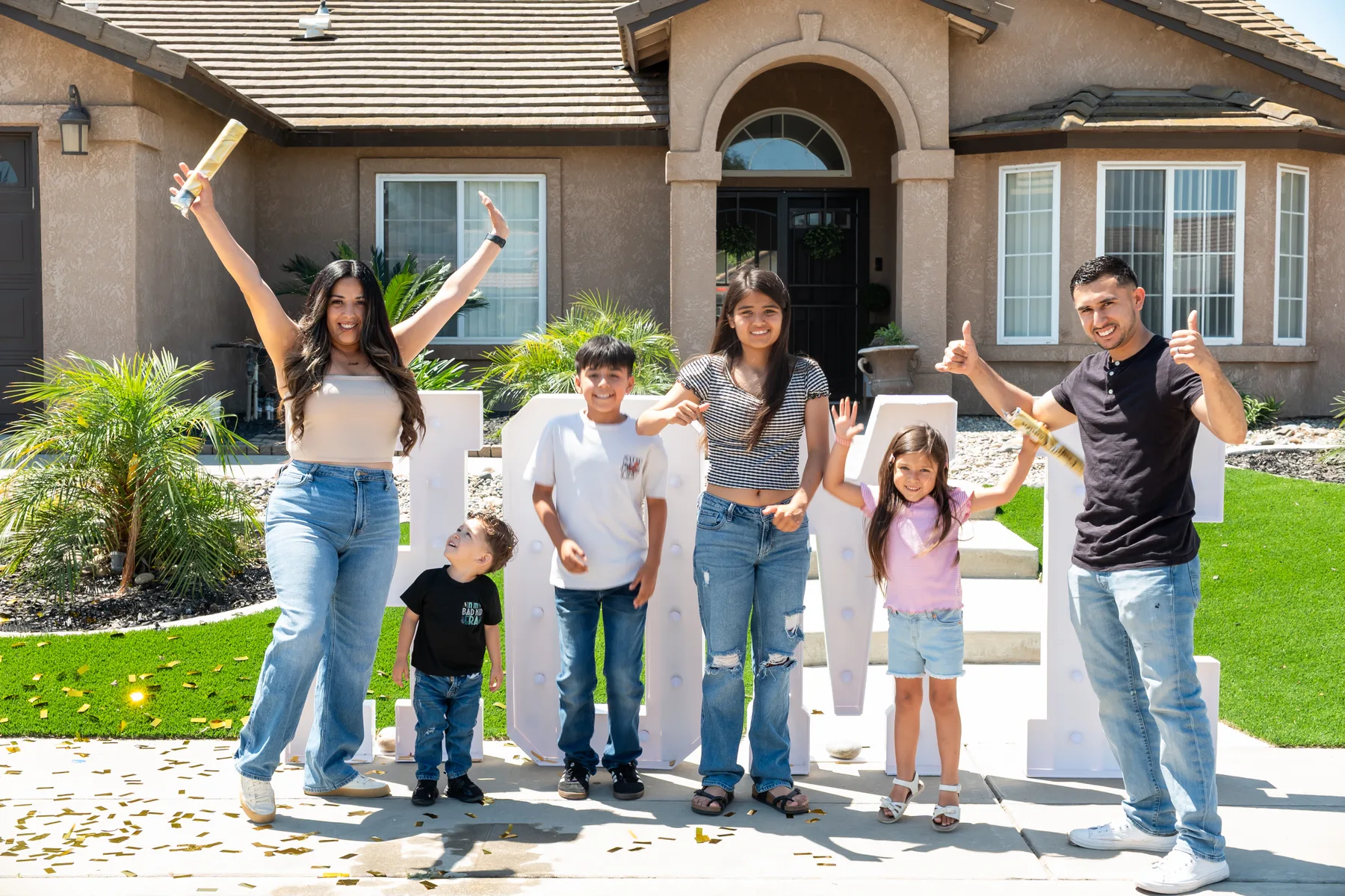 Group raises their arms as confetti falls outside the house.