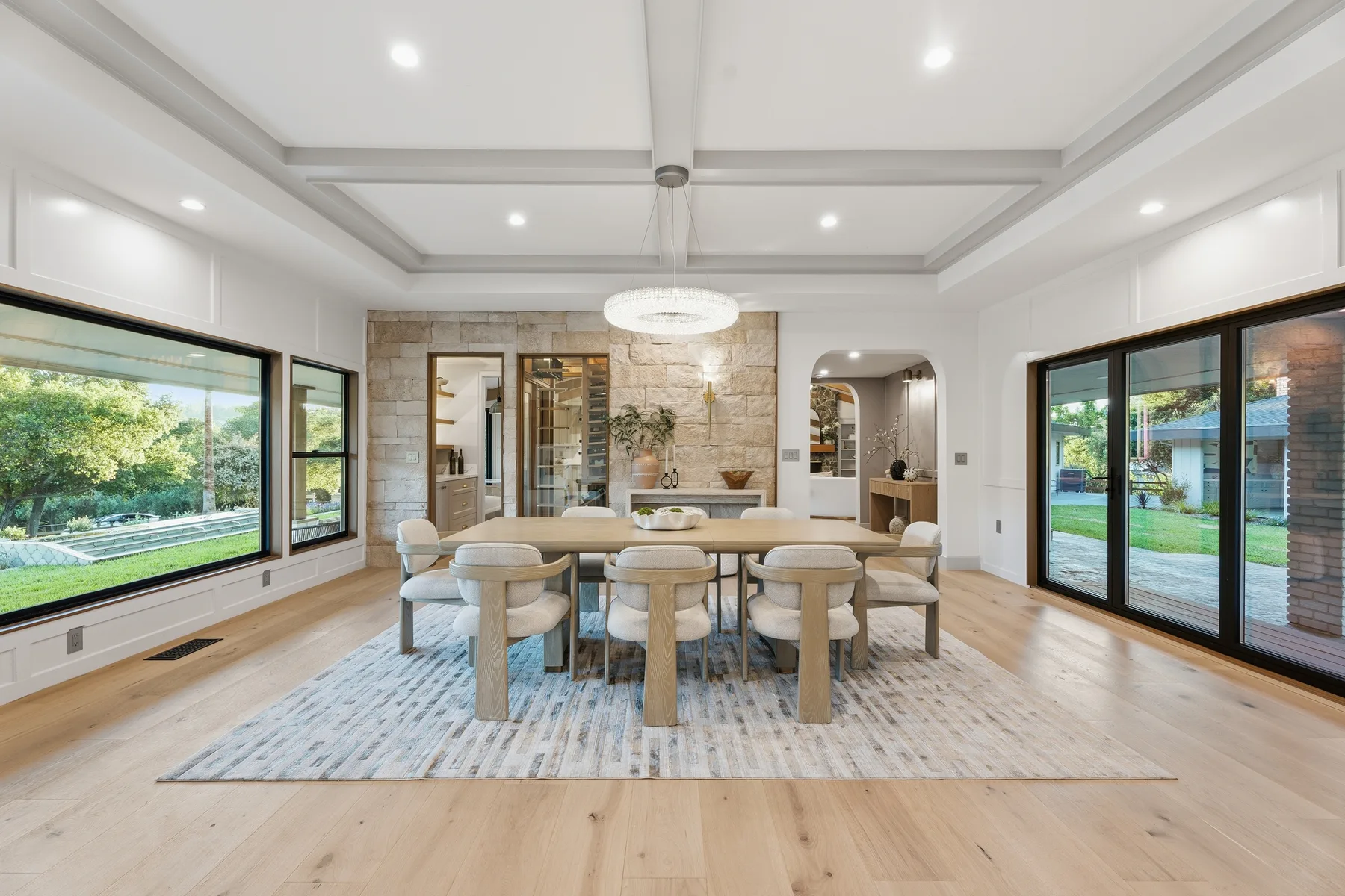 Bright dining room with a stone wall, chandelier, and large windows.
